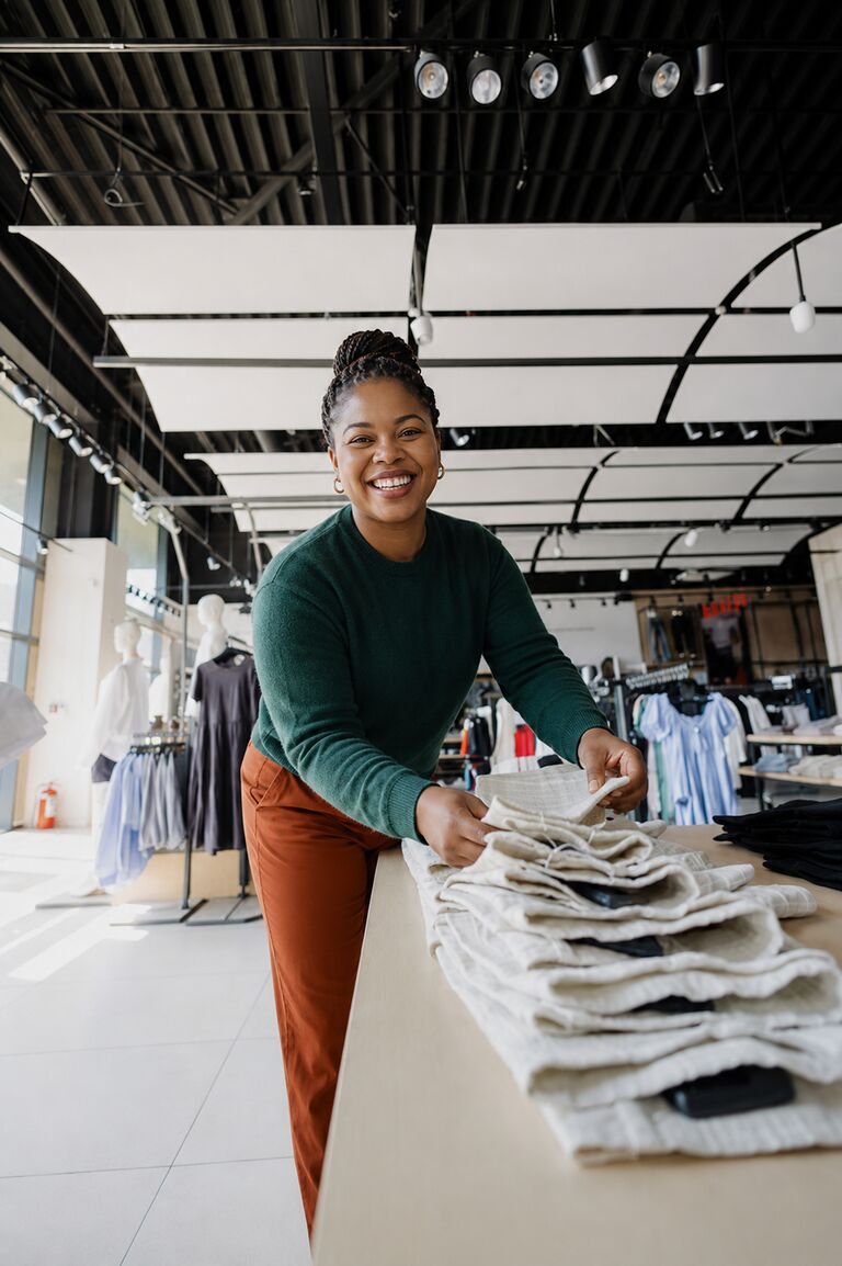 A retail assistant at her counter beneath a sign reading Ubuntu Batho — I am because we are