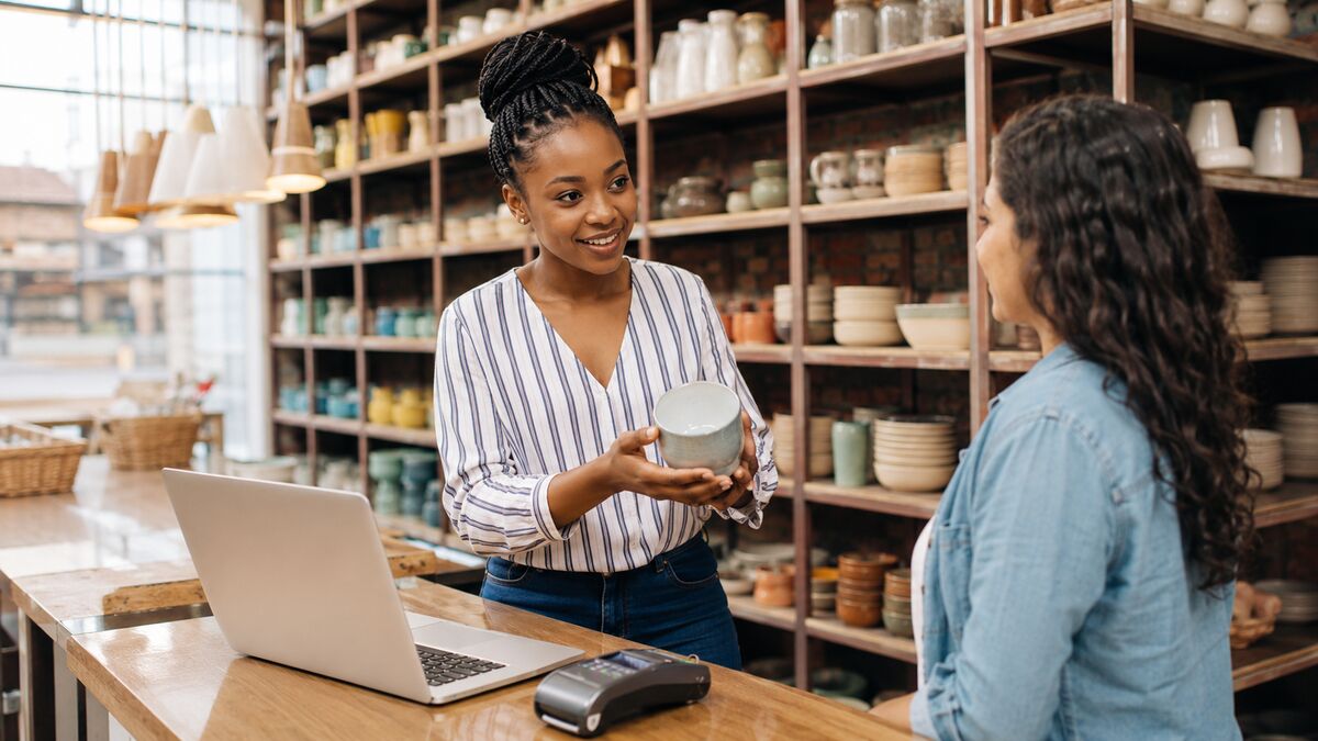 A shop assistant handing a customer a ceramic bowl across the counter